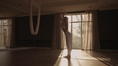 Lens-flare-:A-young-woman-in-white-sportswear-is-stretching-with-a-large-hall-with-large-windows-in-a-slow-motion-scheme-the-sun's-rays-shine-through-the-window.-Healthy-lifestyle-healthy-morning